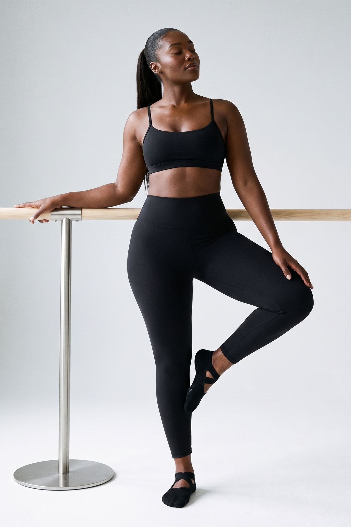 Legging AIKISculpt noir porté à la barre, une jambe repliée, sur fond clair