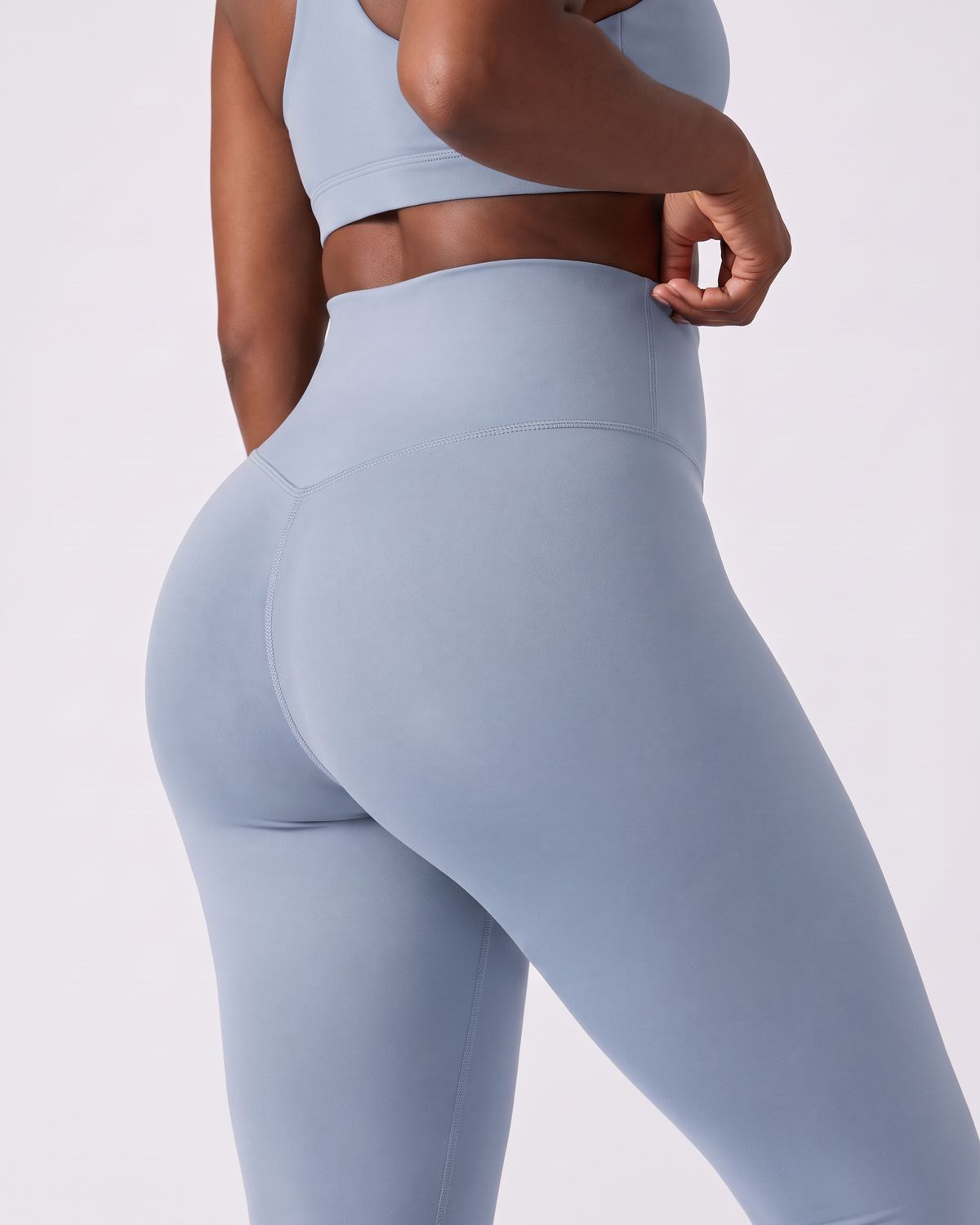 Legging AIKISculpt bleu porté sur fond clair, gros plan de dos sur la ceinture large et le galbe des fessiers