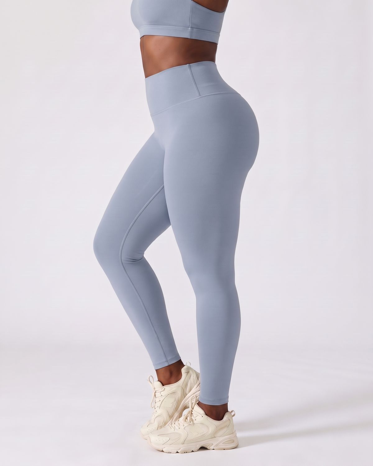 Legging AIKISculpt bleu porté, vu de trois quarts sur fond clair, de la poitrine aux pieds, avec des baskets crème