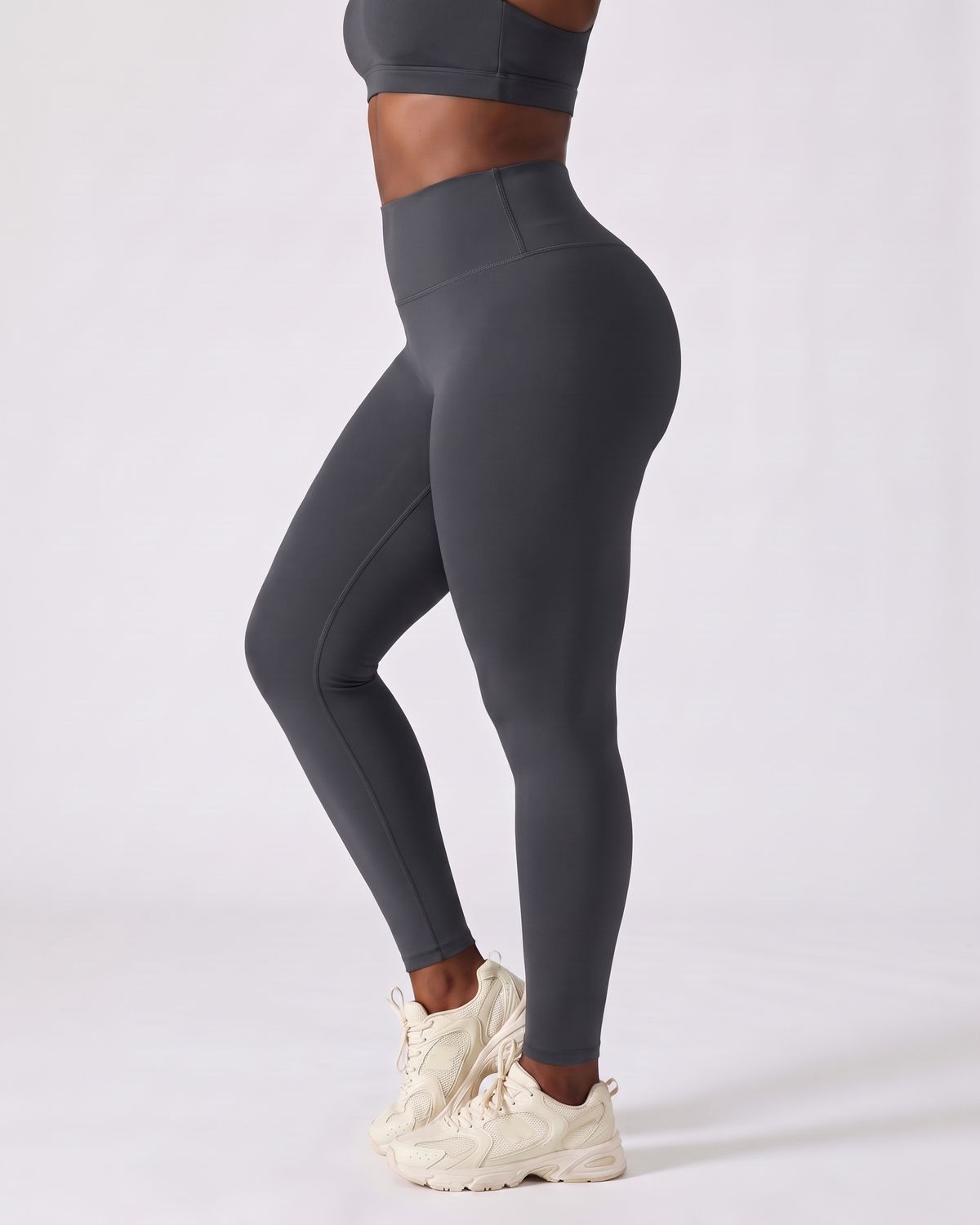 Legging AIKISculpt gris porté, vu de trois quarts sur fond clair, de la poitrine aux pieds, avec des baskets crème