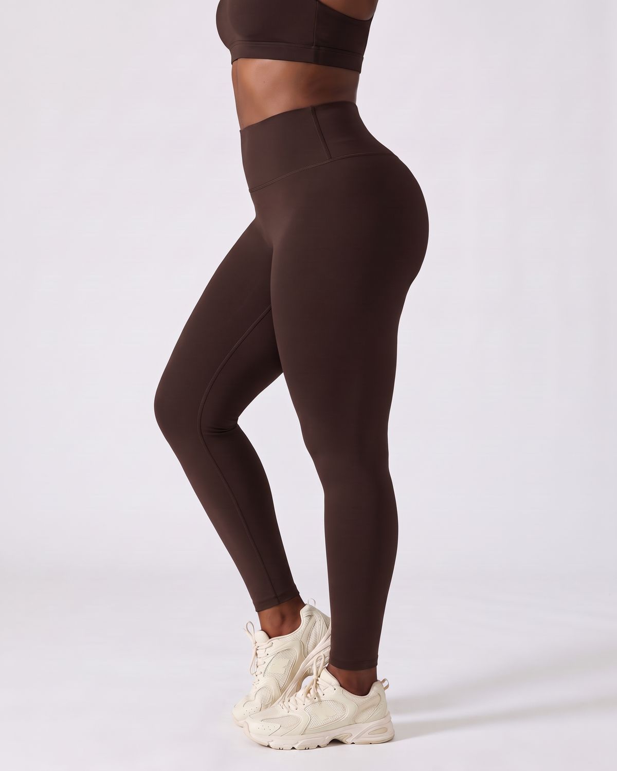 Legging AIKISculpt marron porté, vu de trois quarts sur fond clair, de la poitrine aux pieds, avec des baskets crème