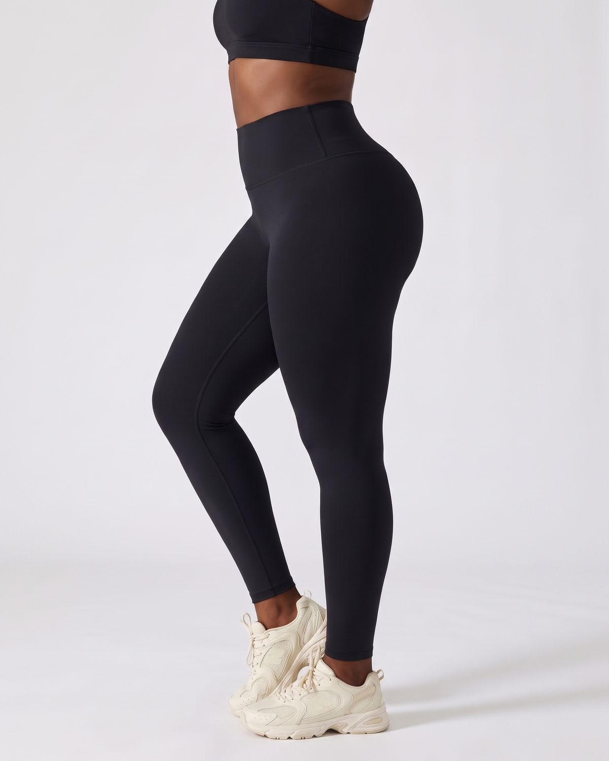 Legging AIKISculpt noir porté, vu de trois quarts sur fond clair, de la poitrine aux pieds, avec des baskets crème