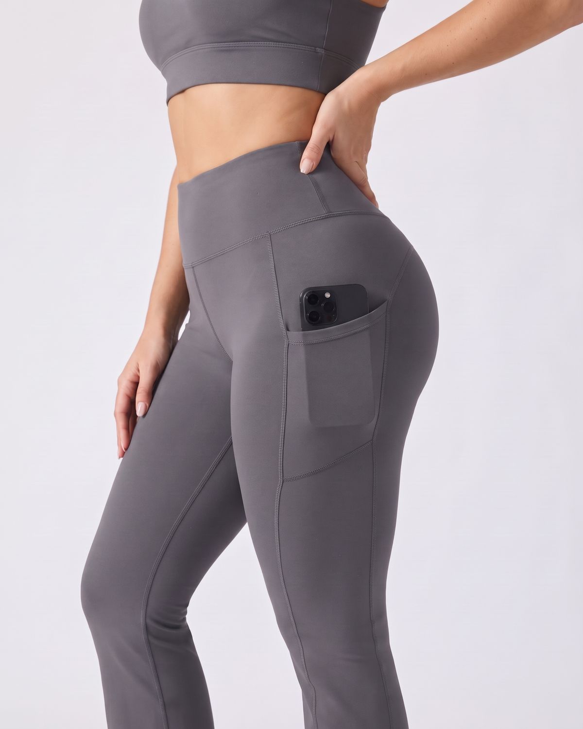 Legging Flare AIKISculpt gris porté sur fond clair, gros plan sur la poche latérale avec un téléphone glissé dedans