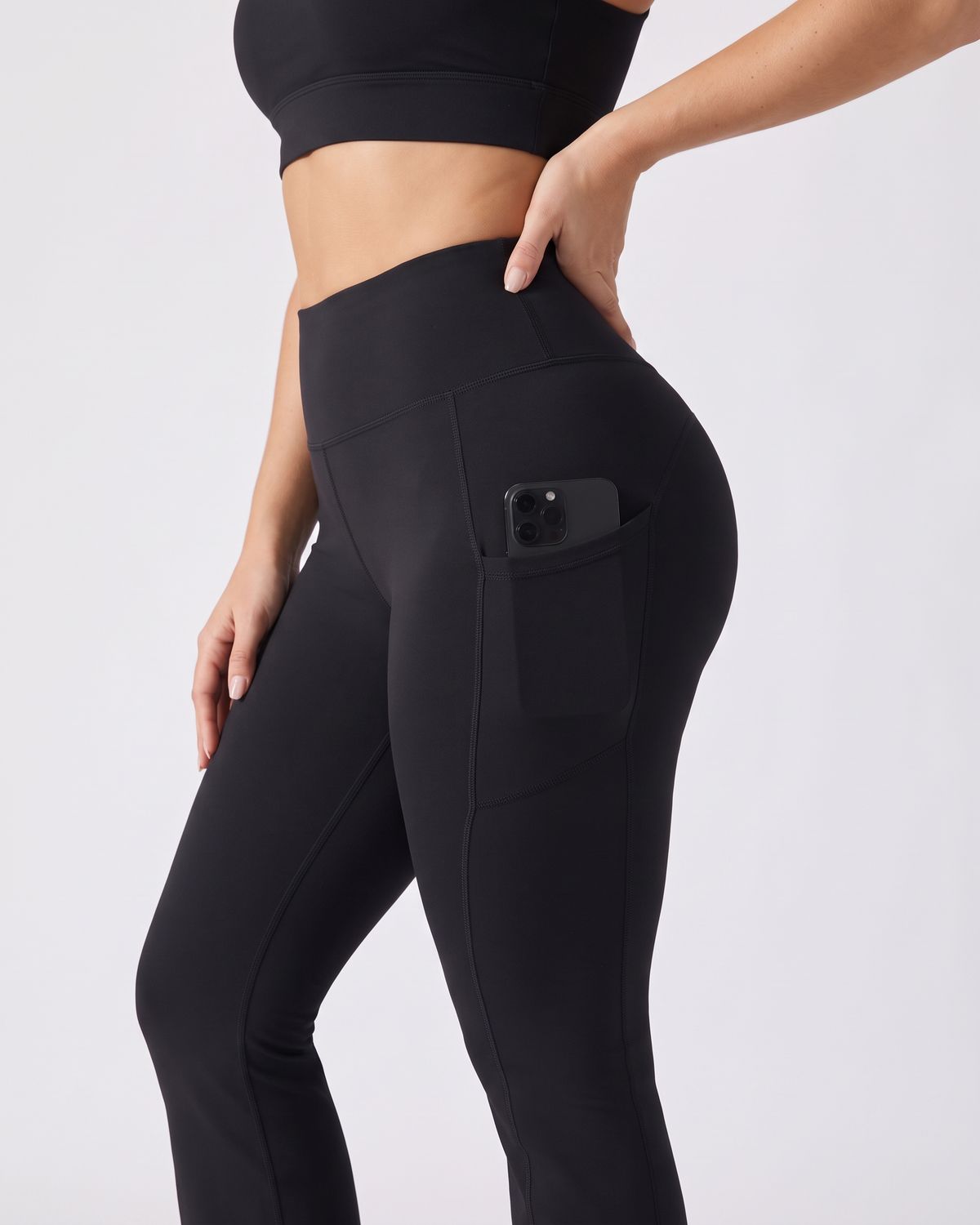 Legging Flare AIKISculpt noir porté sur fond clair, gros plan sur la poche latérale avec un téléphone glissé dedans